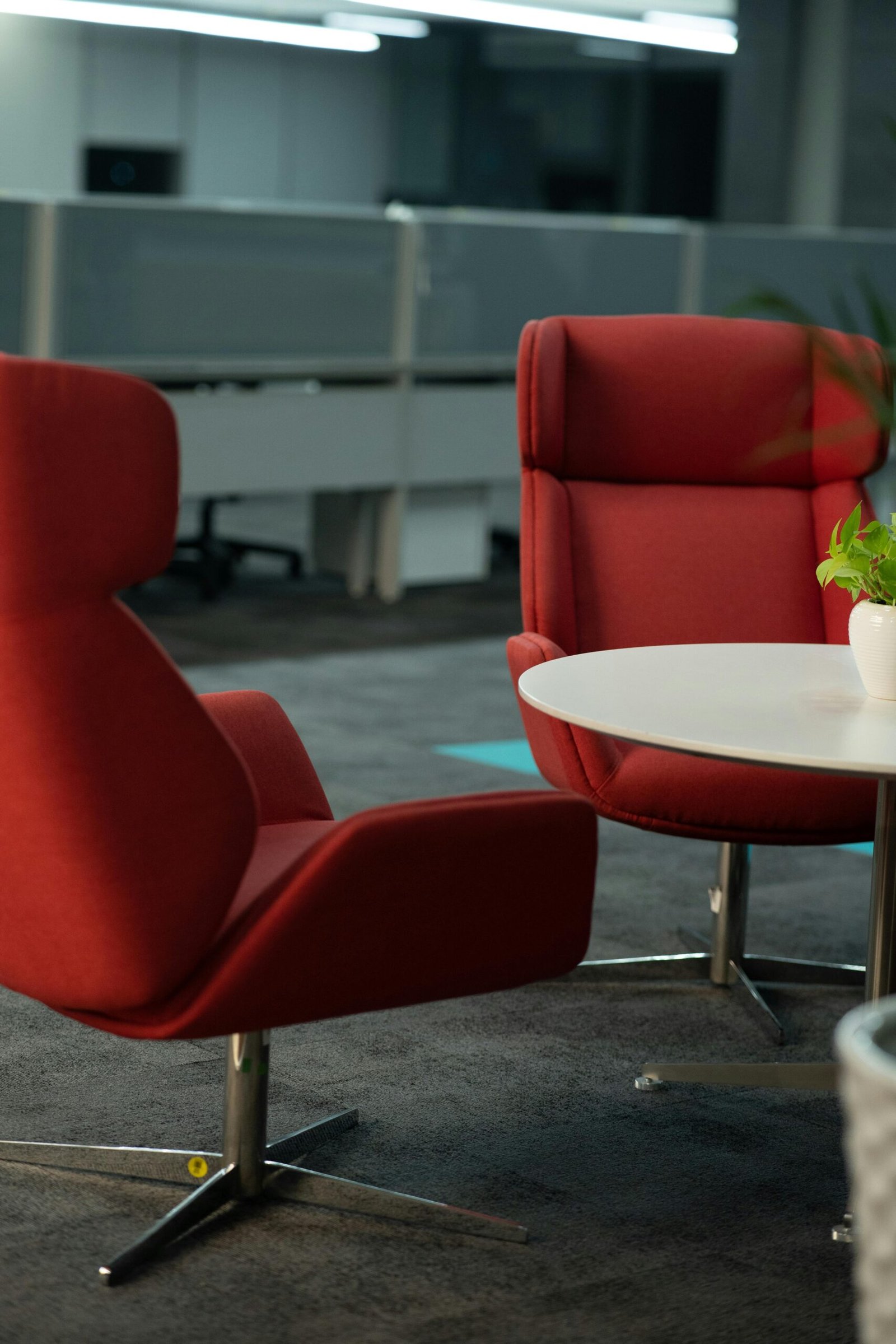 Contemporary office lounge featuring stylish red chairs and a round table, perfect for meetings.